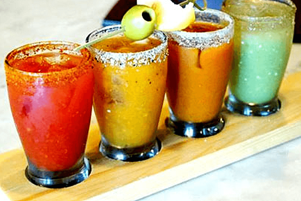A flight of 4 colorful mixed drinks in glasses