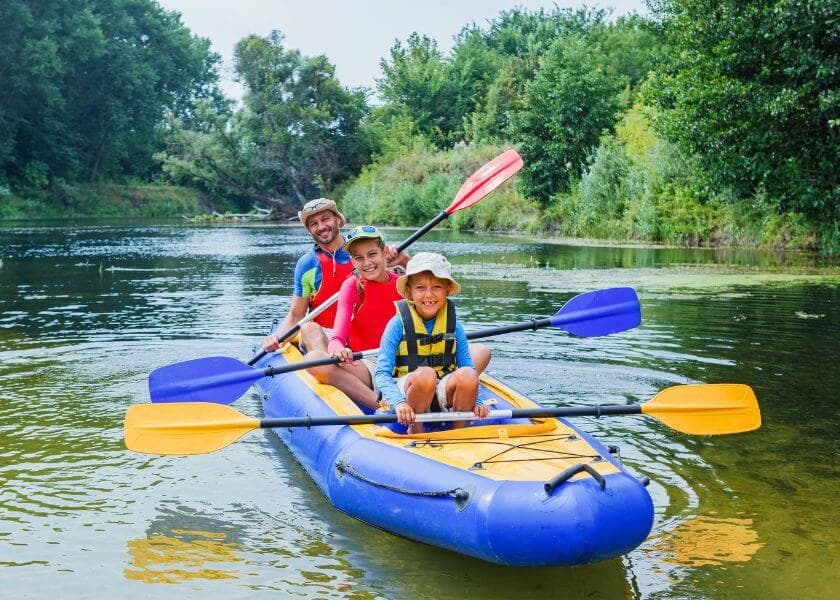 family of three kayaking along river in forested area family of three kayaking along river in forested area